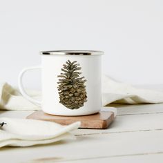 a white coffee mug with a pine cone on the inside sits on a wooden coaster