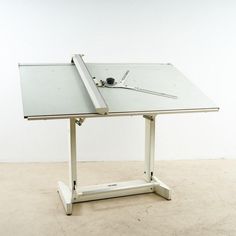 a white table with a glass top and metal frame on the bottom, sitting in front of a white wall