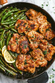 chicken and green beans in a skillet with lemon wedges