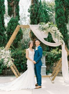 a bride and groom standing in front of an arch decorated with greenery for their wedding ceremony