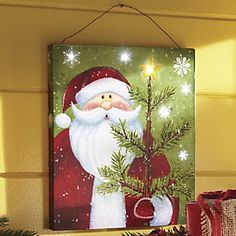 a painting of santa holding a christmas tree on a mantle next to other holiday decorations