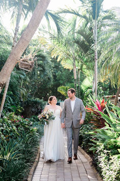 a bride and groom walking through the tropical gardens