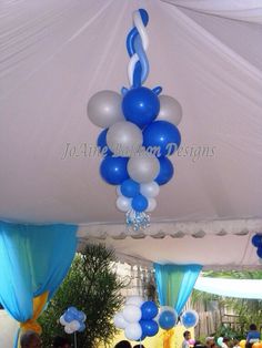 blue and white balloons are hanging from the ceiling in an outdoor party area with people sitting at tables