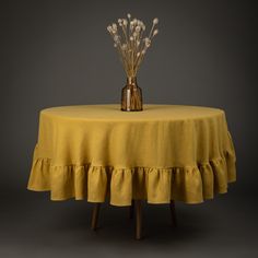 a vase with flowers sitting on top of a yellow table cloth covered table in front of a gray background