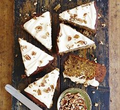 several slices of cake with white frosting and nuts next to a bowl of pecans