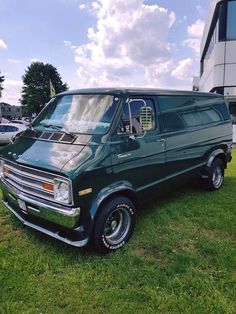 a green van parked on top of a lush green field next to a tall building