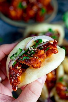 a hand holding up a taco filled with meat and sauce on top of tortilla shells