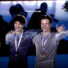 two young men standing next to each other with medals around their neck and hands in the air