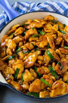 chicken with sauce and green onions in a white bowl on a blue checkered table cloth