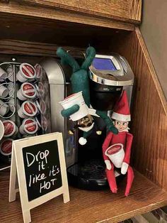 an elf is sitting on the shelf next to a coffee maker and some soda cans