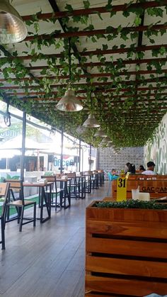 the inside of a restaurant with wooden tables and green plants hanging from the ceiling above