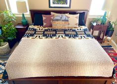 a bed with pillows and blankets on top of it next to two potted plants