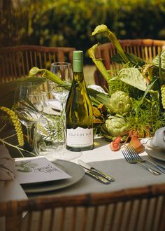 a table set with plates, silverware and wine bottle on top of the table