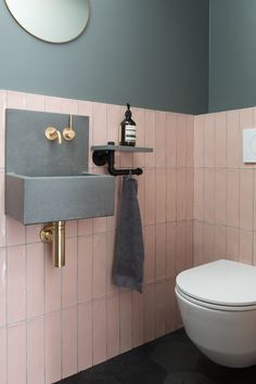 a bathroom with pink and gray tiles on the walls, gold faucet, black towel rack