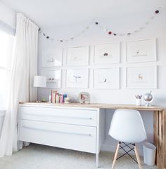 a white desk and chair in a small room with pictures on the wall above it