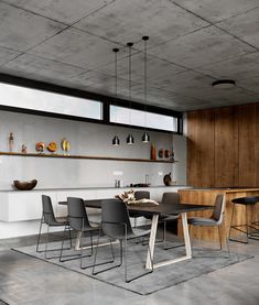 a dining room table and chairs in front of an open kitchen area with large windows