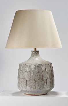 a table lamp sitting on top of a white counter next to a vase with a beige shade