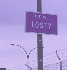 a purple sign that says are you lost? on a pole in front of barbed wire