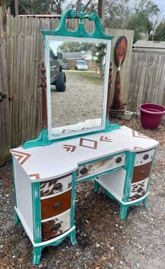 an old vanity with a mirror and drawers in the middle of graveled area next to a wooden fence