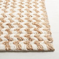 an area rug with white and brown braiding on the top, in front of a wooden floor