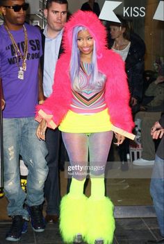 a woman dressed in neon clothing and boots walking down the street with other people behind her