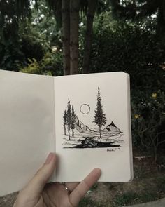 someone is holding up an open book with trees and mountains in the background on it