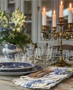 a table set with blue and white plates, silverware and candles