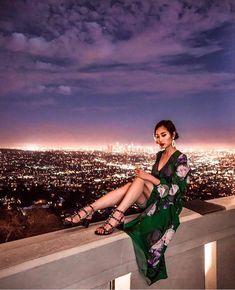 a woman sitting on top of a building next to a cityscape at night