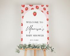 a welcome sign for a baby shower with strawberries on it and greenery in the foreground