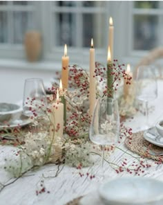 a table topped with lots of candles and flowers next to plates on top of a wooden table