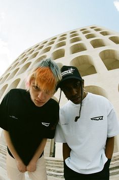 two young men standing next to each other in front of a building