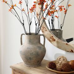 a vase with flowers in it sitting on a table next to a plate and mirror