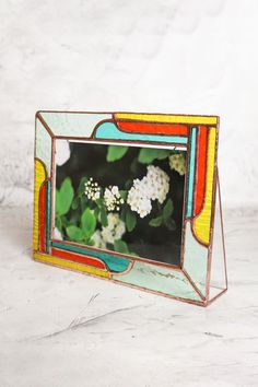 a colorful mirror with flowers in it on a white tableclothed surface next to a wall