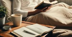 a person sitting on a couch reading a book and holding a cup of coffee in their hand