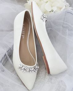 the brides shoes are adorned with crystal brooches and pearled accents, along with a bouquet of white flowers