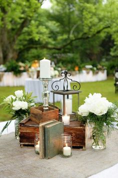 a table with candles, flowers and books on it in the middle of a park