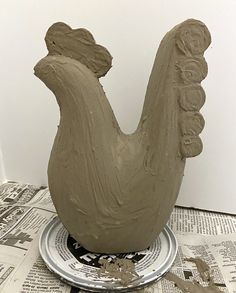 a clay bird sculpture sitting on top of a metal plate next to a newspaper page