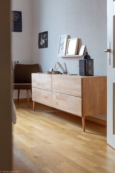 a wooden dresser sitting on top of a hard wood floor next to a wall filled with pictures