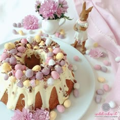 a bundt cake with white icing and pink candies on it sitting on a plate