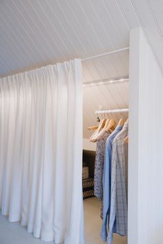 an open closet with clothes on hangers and white curtains hanging from the ceiling in front of it