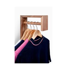 three shirts hanging on wooden hangers in front of a white wall and two pink ones