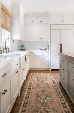 a large rug in the middle of a kitchen with white cupboards and drawers on both sides