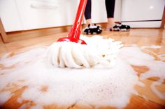 a person is cleaning the floor with a red mop and white fluffy cloth on it