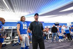 two football players are talking to each other in the locker room while others look on