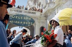 a woman is holding flowers in front of a building with people taking pictures onlookers