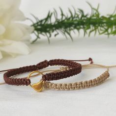 two bracelets with gold heart charms on white cloth next to green plant and flower