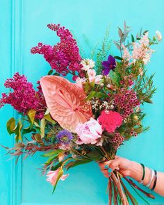 a person holding a bouquet of flowers in front of a blue door with green leaves