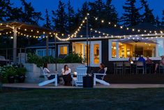 people are sitting at tables outside in the evening with string lights strung across the patio