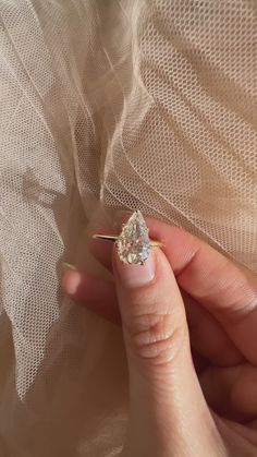 a woman's hand holding an engagement ring with a diamond in it on top of a veil