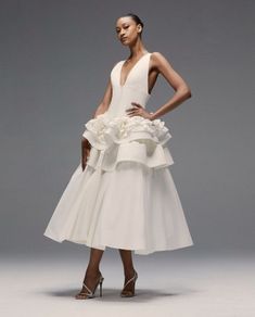 a woman wearing a white dress with flowers on the skirt and heels, standing in front of a gray background